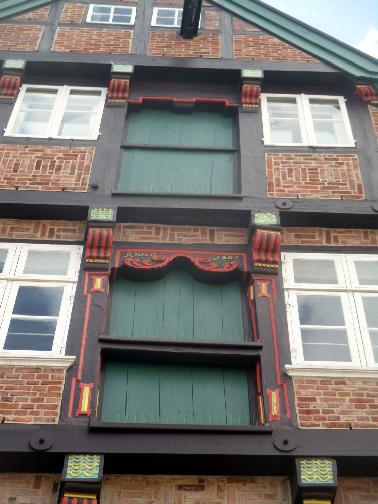 Ein Fachwerkhaus aus Backstein. Der Fokus des Bildes liegt auf zwei grünen geschossenen Ladeluken unter dem Dach.