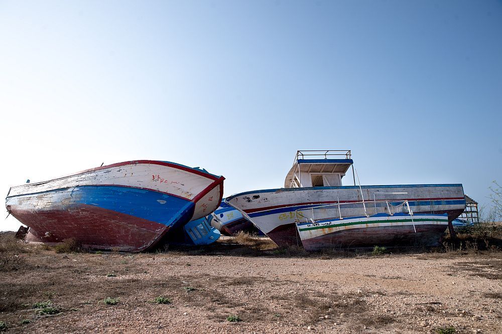 Boote liegen im Wüstensand. Im Vordergrund sind zwei Holzbppte zu sehen die mit dem Bug zueinander liegen, und dahinterliegende weitere Boote verdecken. Das rechts bot ist weis blsu rot gestrichen das linke in weis und blau.