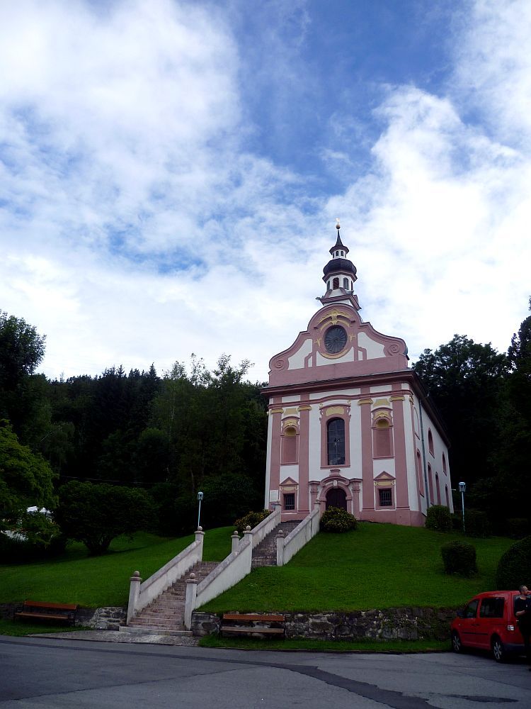 Die Rokokokapelle vom Mentlberg von der Seite. Der Hügel mit der grauen Steintreppe, die zu ihr führt, sind deutlich zu sehen.