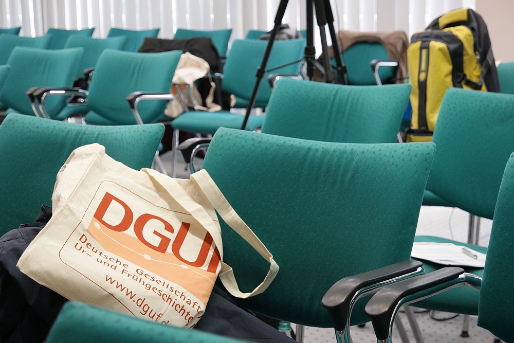 Der leere Raum mit den grünen Stühlen. Eine DGUF-Tasche liegt auf einem Stuhl.