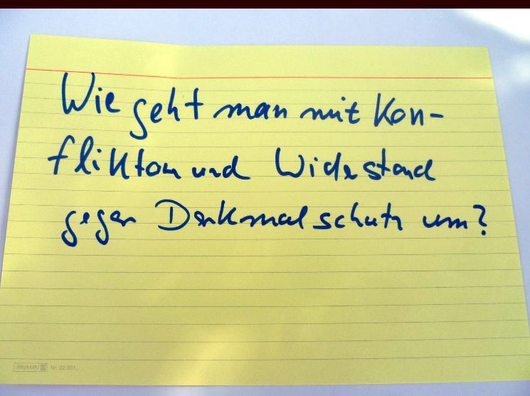 Eine gelbe Karteikarte mit der Aufschrift: Wie geht man mit Konflikten und Widerstand gegen Denkmalschutz um?