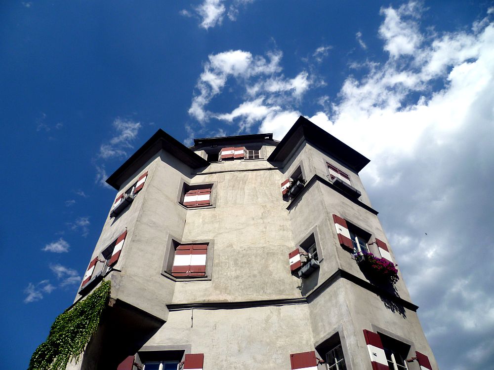 Die Ottoburg. Ein grauer Burgturm mit zwei großen Erkern. Daran Fenster mit geöffneten weis rot gestrichenen Fensterläden aus Holz.