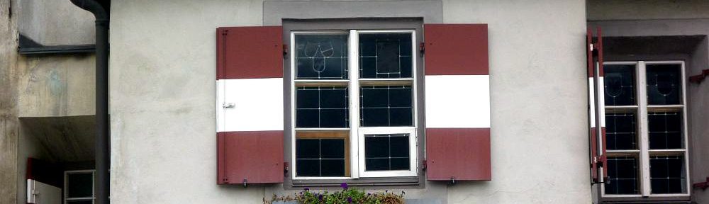 Ein Erker aus grauem Stein. Es gibt ein Fenster mit weiß-roten Fensterläden. Darunter ein Schild mit dem Namen "Ottoburg"