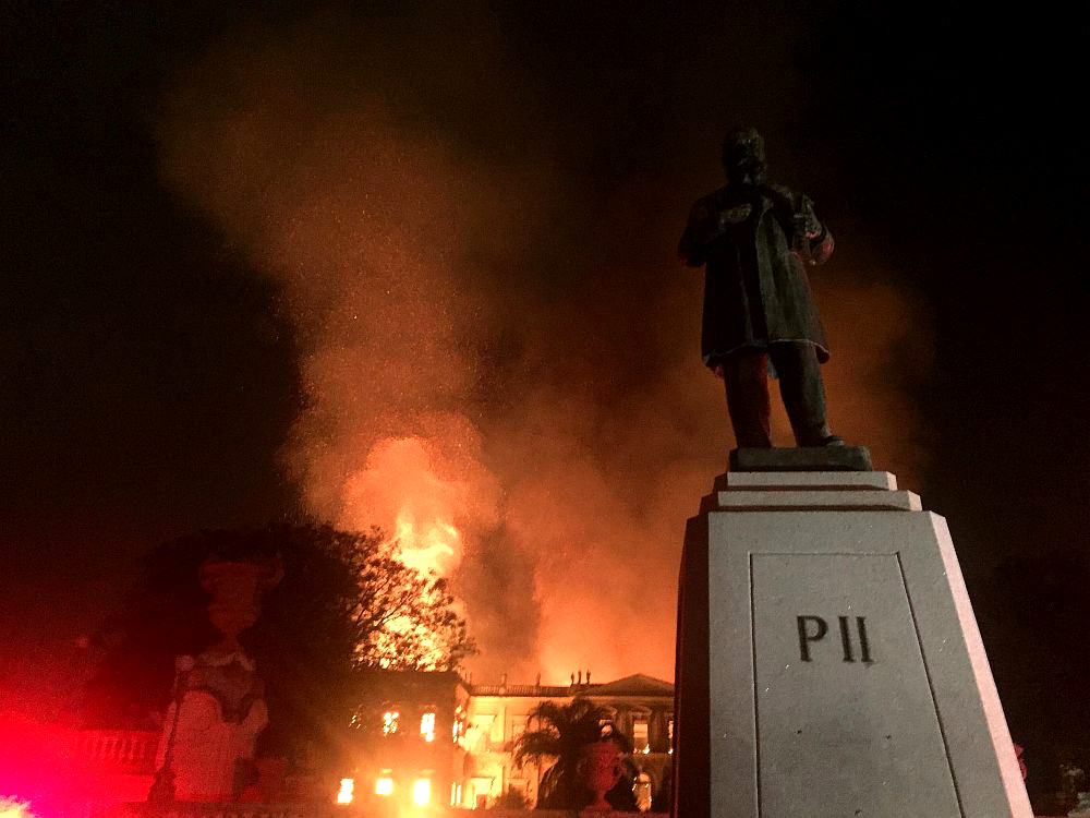 Eine Statue von Phillip dem zweiten im Vordergrund - er ist im Dunkeln kaum zu erkennen. Dahinter brennt lichterloh und kilometerweit sichtbar sein ehemaliges Schloss, das als Nationalmuseum genutzt wurde.