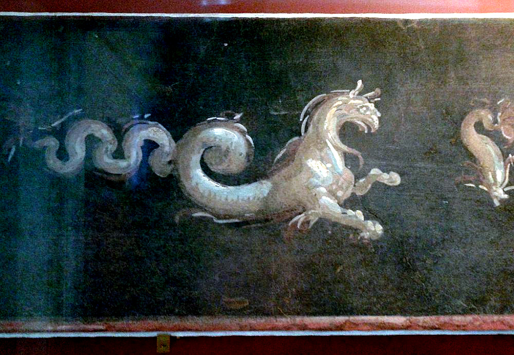 Wandmalerei: Oben und untern ein roter Rand, dazwischen dunkelblaue Grundierung. In der mitte ein helles Grefenwesen, mit einem langen Schwanz, vielleicht auch eine Art Drachen.