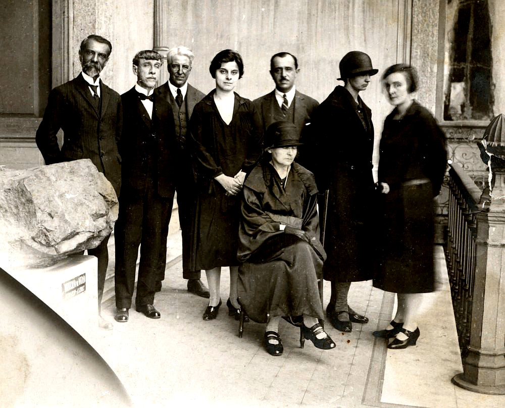 Gruppenbild Schwarz-Weis.8 Personen, darunter 4 Frauen, alle Stehen, nur eine Frau sitzt auf einem Stuhl.