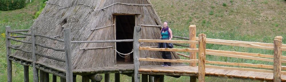 Eine Hütte auf einem Holzpodest. Die Hütte besteht aus nur einem Geschoss, das gleichzeitig ein Dachgeschoss mit einem Giebel ist. Dieses Dach ist mit Stroh gedeckt. Die Tür befindet sich an der Giebelwand.