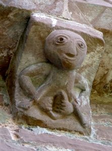 Steinreleif das eine Sheela Na Gig zeigt. Die Glatzköpfig Frau ist Nackt, und hält ihre Schamplippen umklammert.