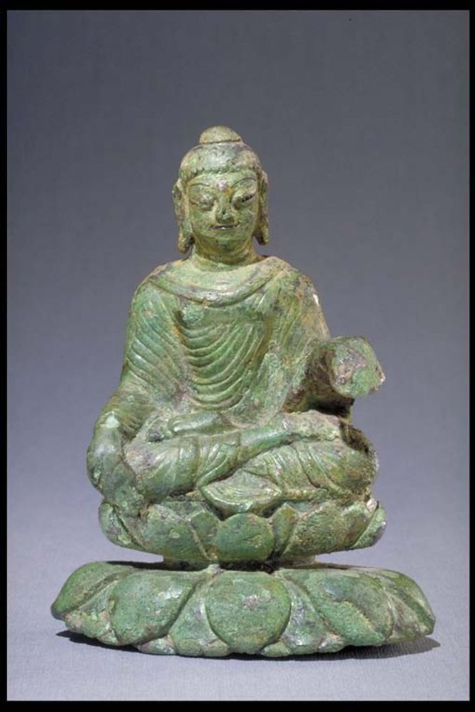 Eine Buddhastatue aus Grünem Jadegestein. Der Buddha sitzt im Lotossitz. Die Linke hand ligt auf sinem Knie, die rechte ist erhoben aber abgebrochen.