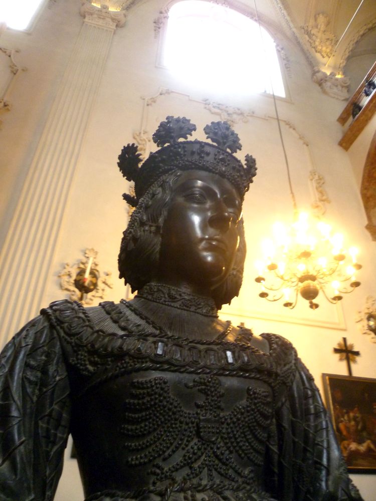 Eine schwarz-Braune Bronzeskulptur. Ein Frau mit einer Königskrone in einem aufwändigen Gewand.