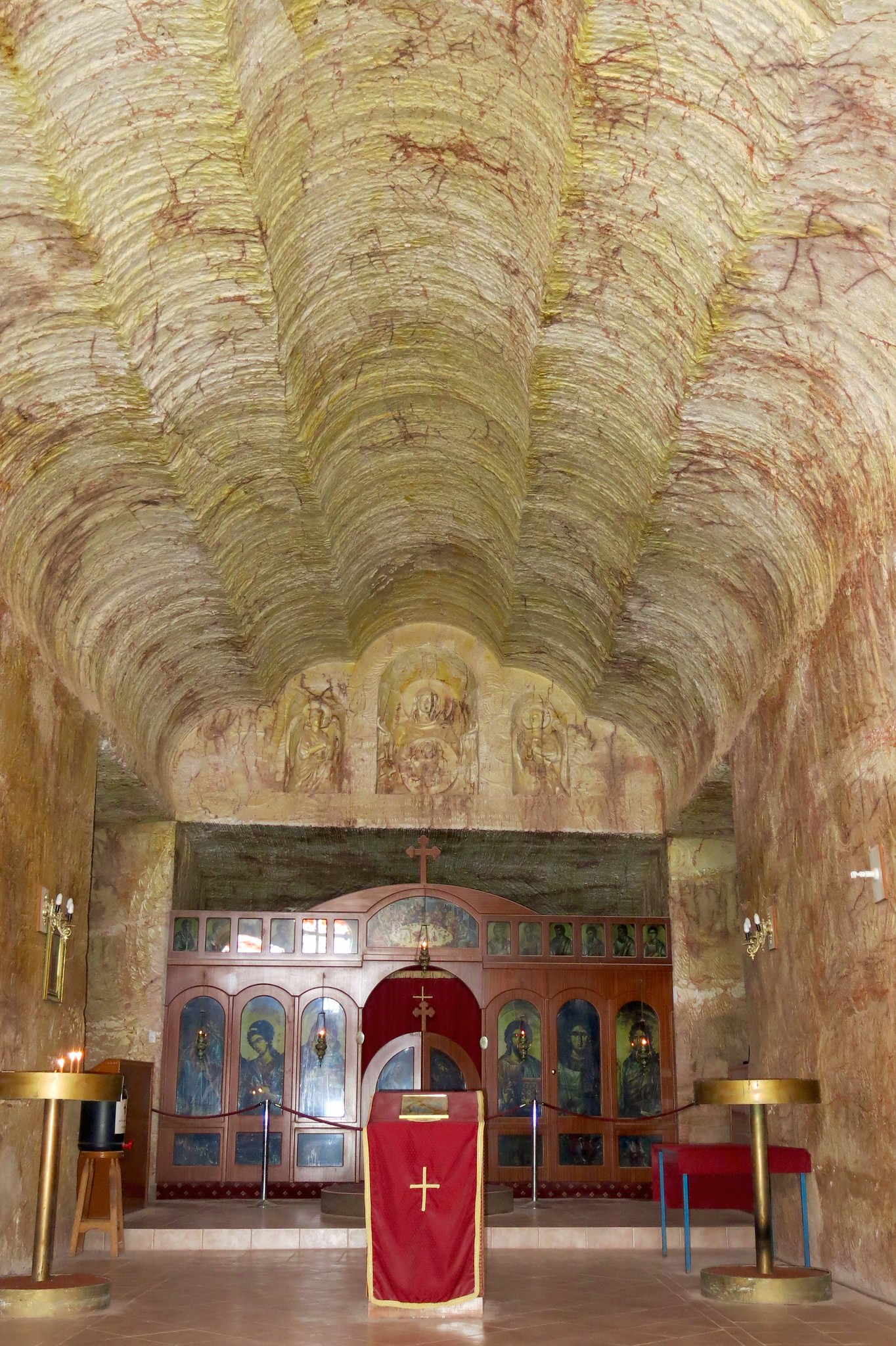 Die Kirche Von Coober Pedy. Ein SHolzfertäfelter Altar ist in den Stein eingelassen. Eiligenbilder sind zu sehen. Das Gewölbe ist nahezu Wolkenförmig gestalltet.