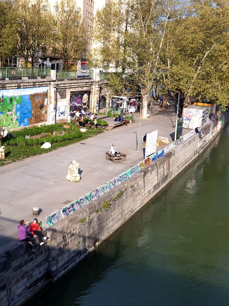 Blick auf de Agora in Wien. Ein kleier Garte, eie Frau legt der Soe, viele Skulpture stehen drum rum.