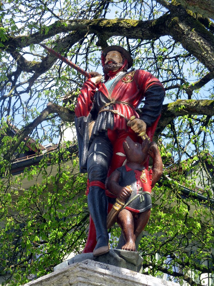 Berner Brunnenfigur eines Mannes mit einem braunen Bart. Es handelt sich um einen Wanderer mit Wanderstock und Bündel. Er trägt blau-rote Kleidung, und ein Bärenkind begleitet ihn.