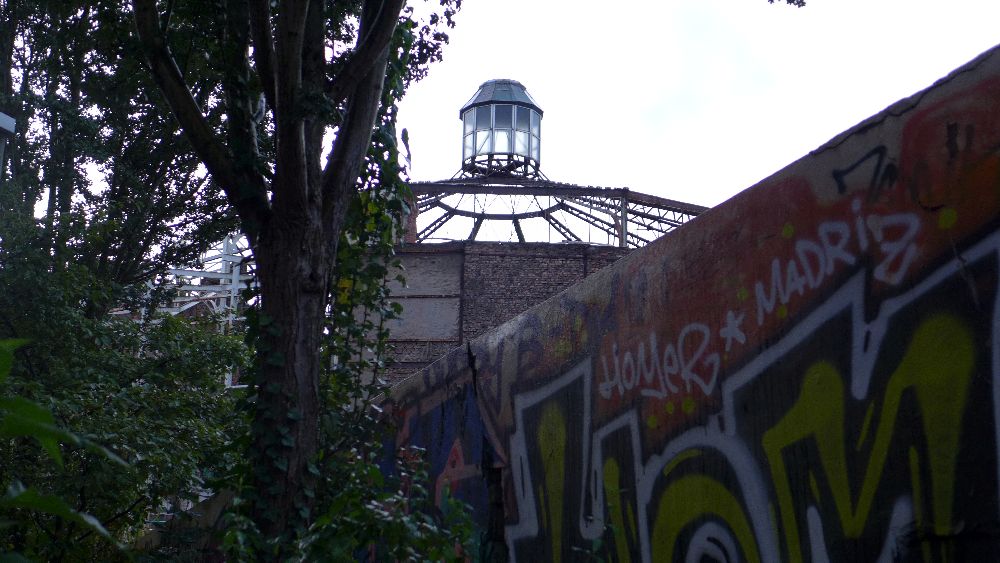 Ein Baum eine angesprayte Wand. Daheimter erhebt sich der Lauechtturm der Schilleroper.