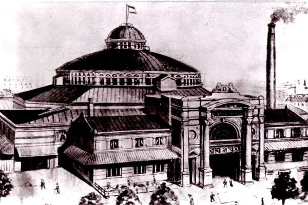 Ein Großes Zirkusgebäude mit Doppeldach. Es ist Rund und hat einen gigantischen Vorbau im stile der Gründerzeit.