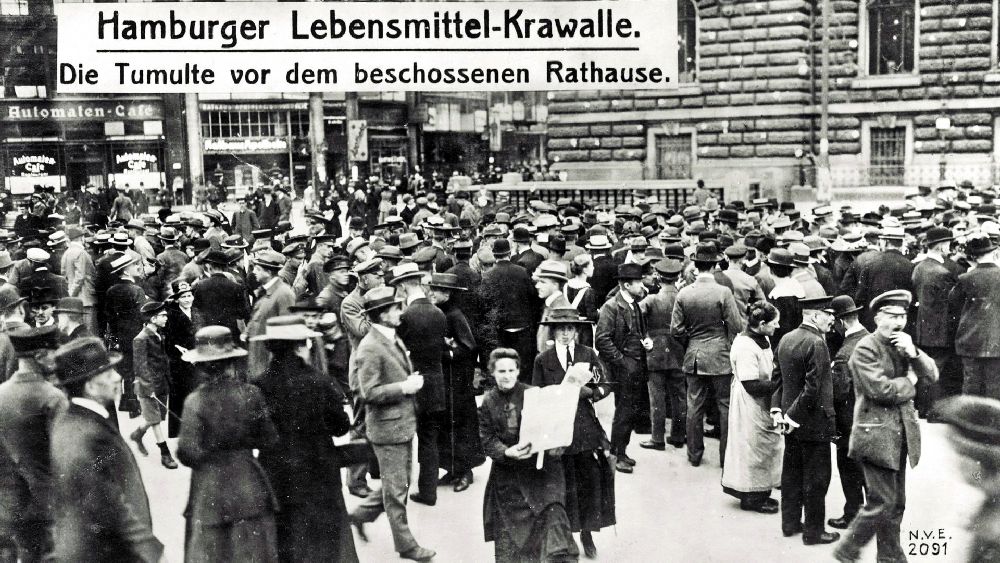 Eine Menschenmasse vor dem Hamburger Rathaus auf einem Schwarzweißbild. Eine Aufschrift verlündet: "Hamburger Labensmittel-krawalle vor beschossenen Rathaus"