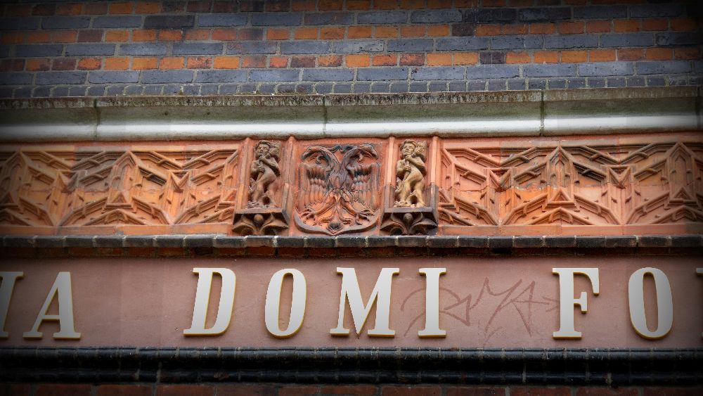 Das Umlaufende Terrakottafries mit symetrischen mustern in der Mitte zwei Jungen die den Lübecker Doppelkopfadler säumen. Die Jungen haben verschiedene Farben.