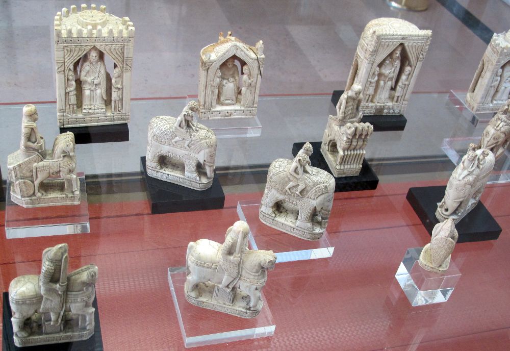 Geschnitzte Figuren vmtl. Elfenbein. In der Mitte sind zwei aufwändig gestaltete Elefanten zu sehen, und im Hintergrund opulente Figuren, die den König und die Königin zeigen.