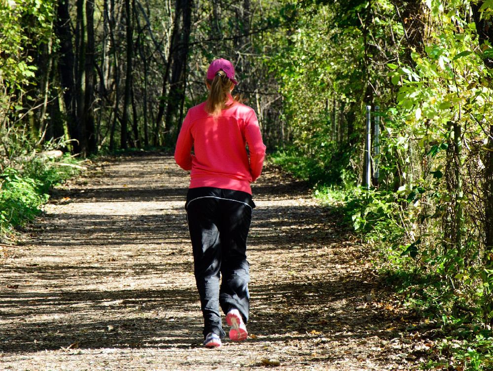 Eine Frau beim gemütlichen Joggen im Wald von hinten.