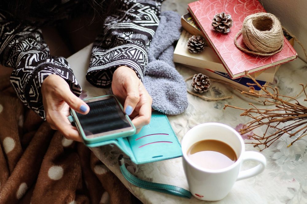 Die Hände einer Frau, die ein Handy bedienen, neben einem Café.