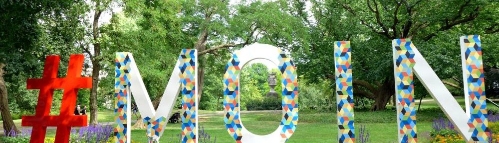 Ein riesiges Denkmal, das sie Schrift #Moin bildet vor einem Park mit vielen Blumen.