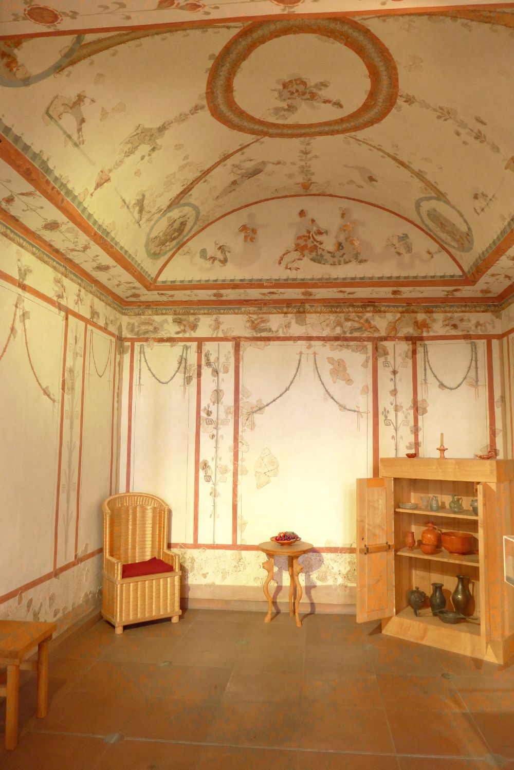 Ein Raum mit Floraler Wandmalerei. Ind er ecke steht ein Korbstuhl, im der anderen Ecke ein Bücherregal.