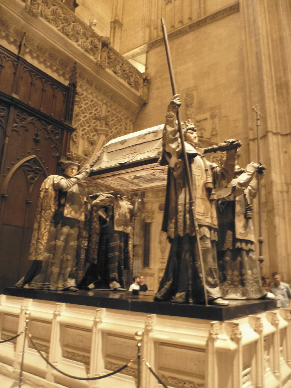 Eine riesiege Skulptur aus vier Skulpturen die eine Bahre mit einem Sarg tragen.