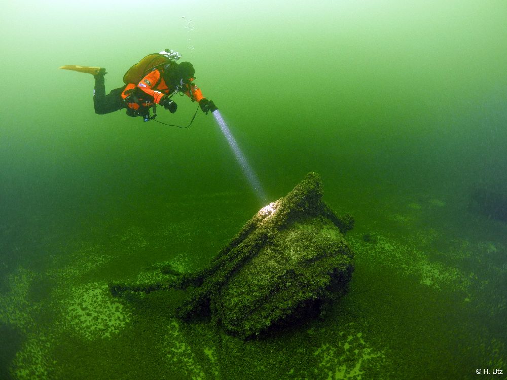 Taucherin im Roten Taucheranzug leuchtet ein Schiffswrack an.