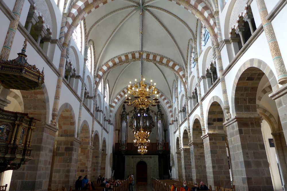 Blick durch das Mittelschiff auf die Orgel. Links und rechts sind Säulen, ein umlaufender Gang und darüber gotische Fenster.