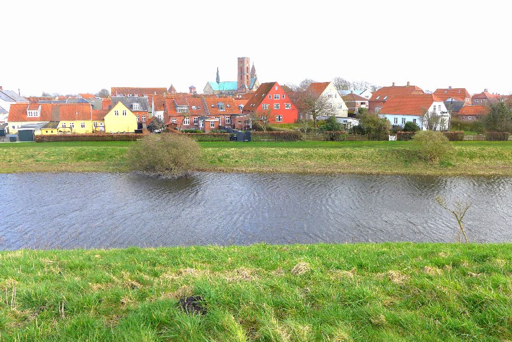 Hinter einem Kanal niedrige Häuser in bunten Farben, in der Mitte eine Domkirche mit zwei Türmen.