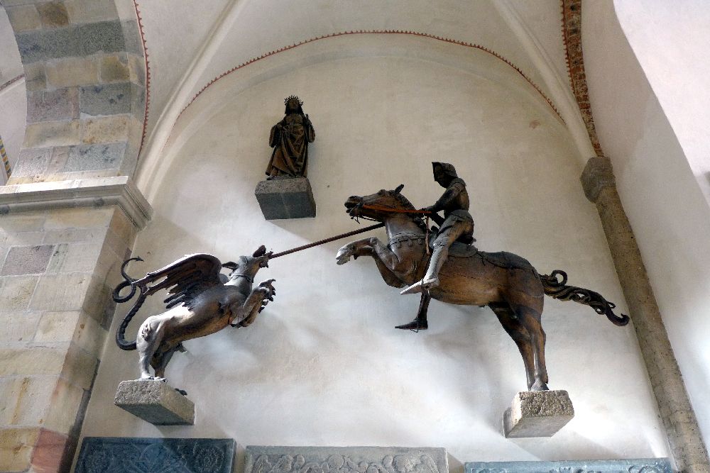 Eine Holzschnitzerei von einem Ritter auf einem Pferd, der mit einer Lanze einen Drachen angreift