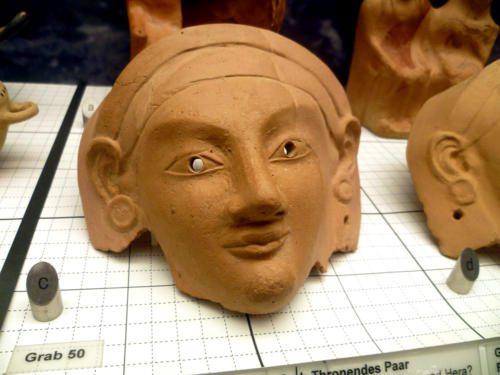 Weibliche Maske mit durchbohrten Augen aus Terrakotta. Es handelt sich um einen Grabfund